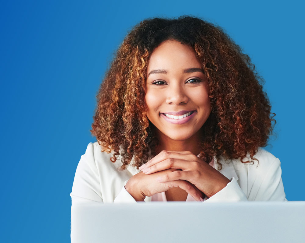 Photo of a woman with laptop, notepad and coffee cup, sitting against a blue background.