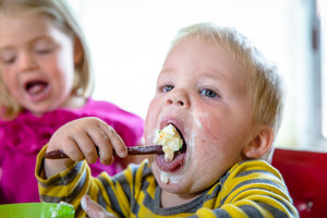 little toddler taking a huge bite with a wood teething spoon - Earlywood